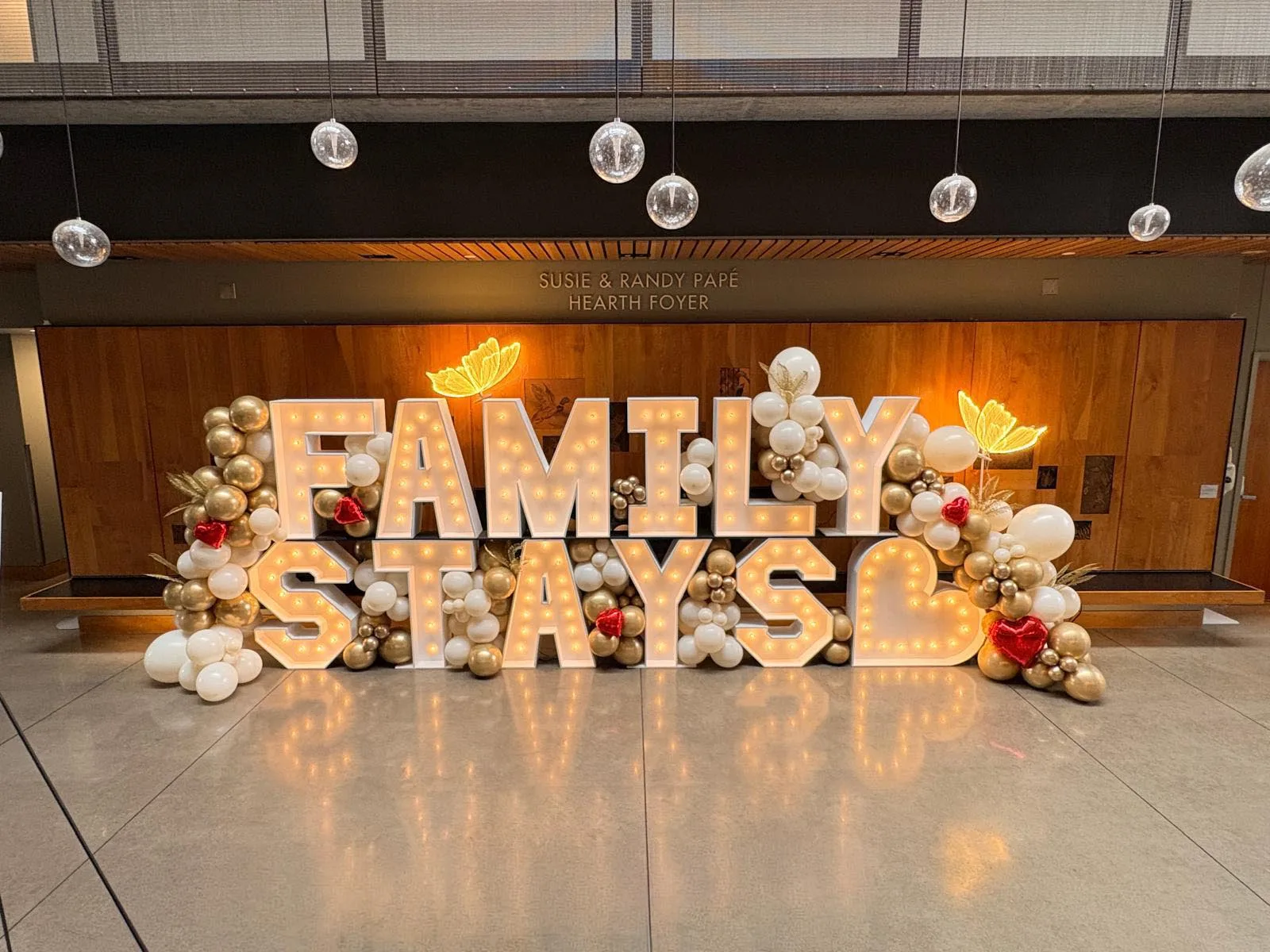 Illuminated “FAMILY STAYS” marquee letters with a white heart, surrounded by cream, gold, and red balloon décor for Ronald McDonald House Oregon’s 2026 Hope-Raiser Gala in Eugene, Oregon by Salem Balloons and Flowers.