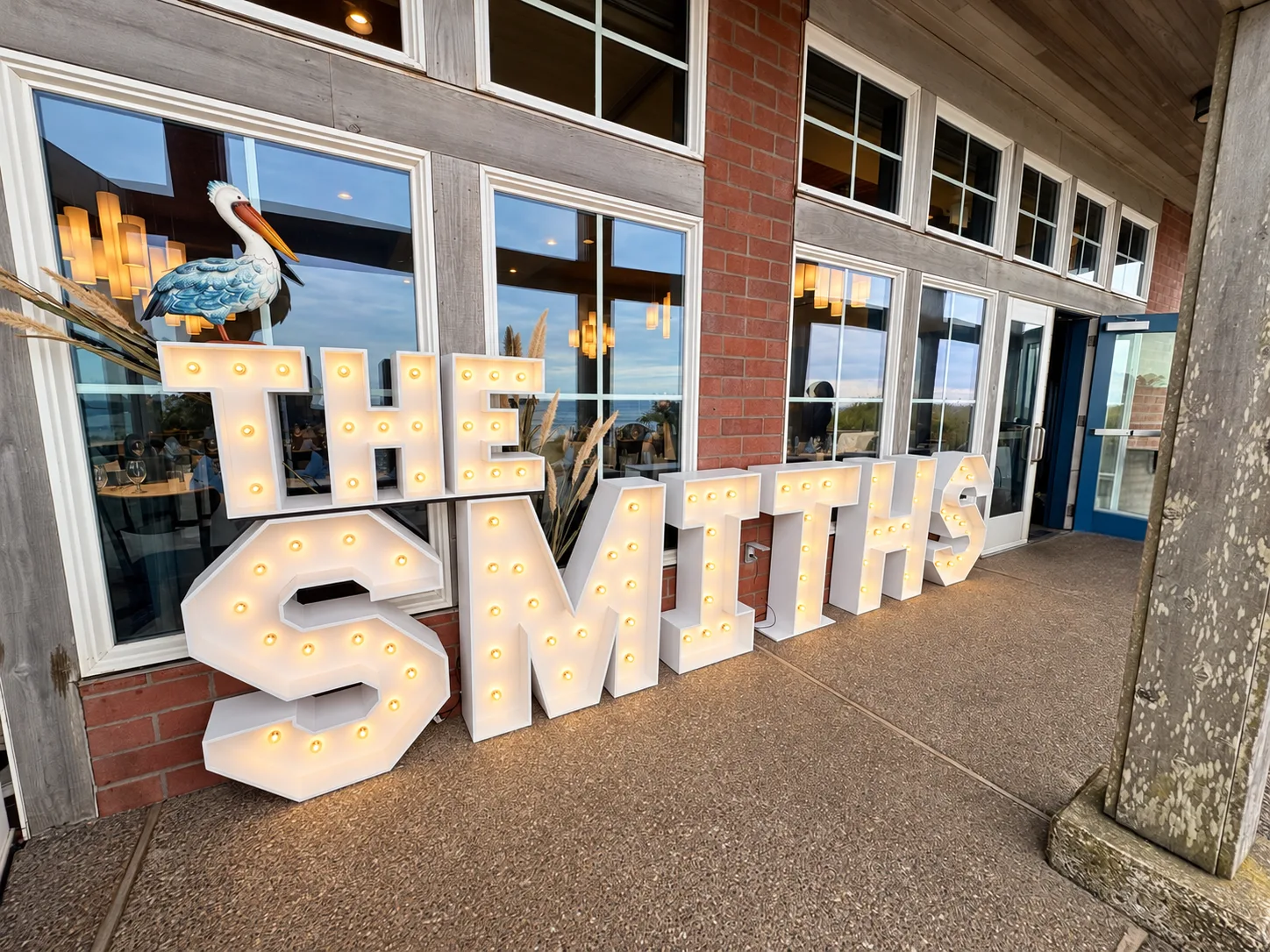 Illuminated THE SMITHS wooden marquee letters displayed on the covered porch at Pelican Brewing for an Oregon Coast wedding in Pacific City, Oregon, by Salem Balloons & Flowers.