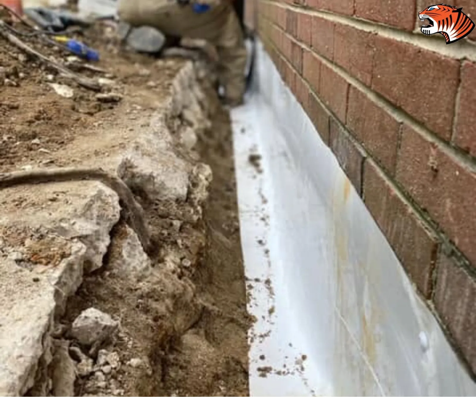 White waterproof membrane barrier lining the excavated foundation wall of a brick home.