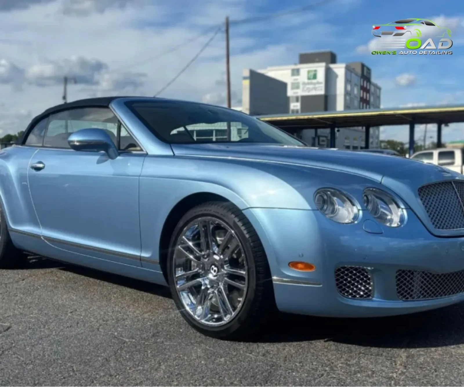 Front three-quarter view of a light blue Bentley convertible parked in an open lot.