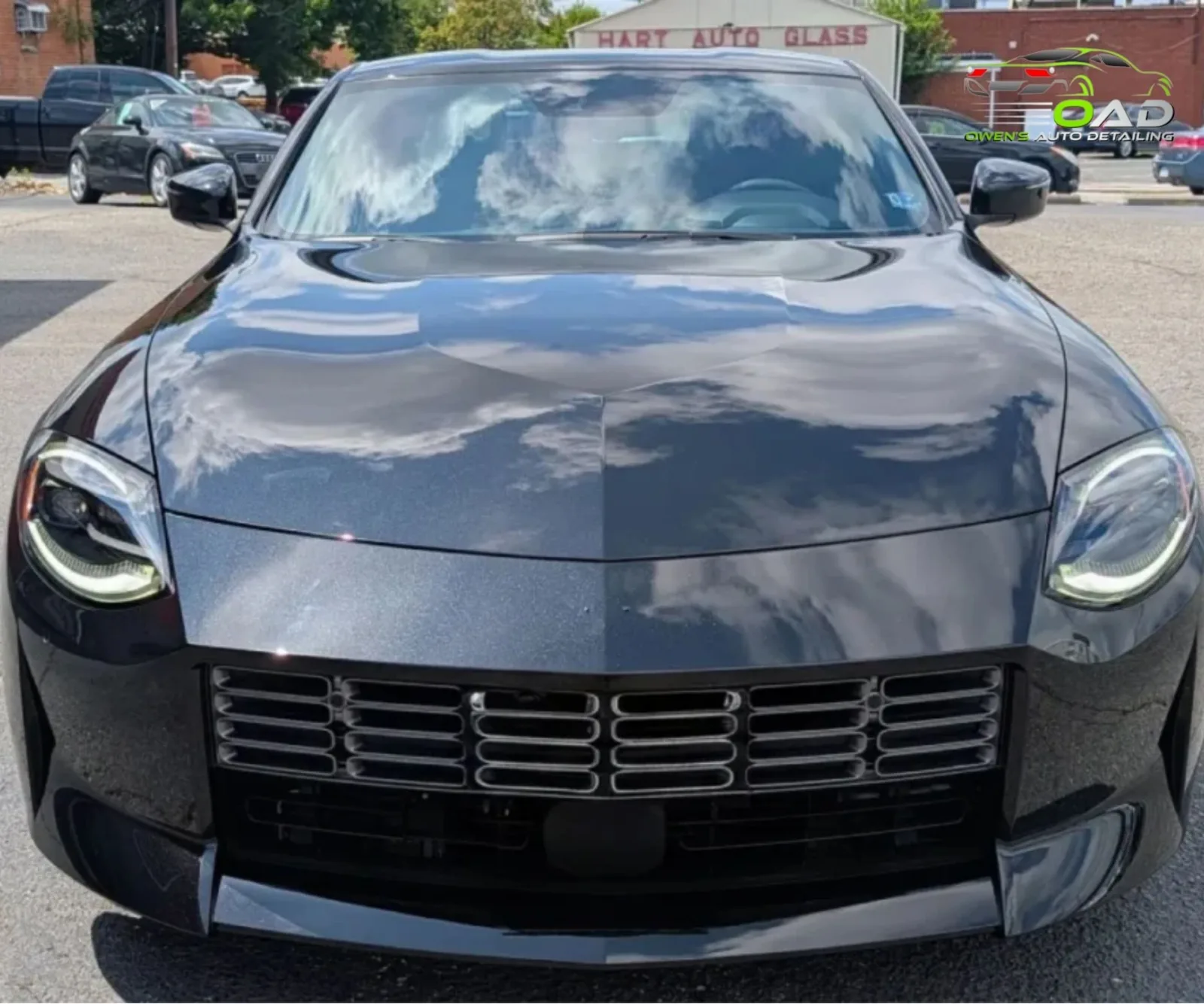 Direct front view of a dark metallic grey Nissan Z showing a clear cloud reflection on the hood.