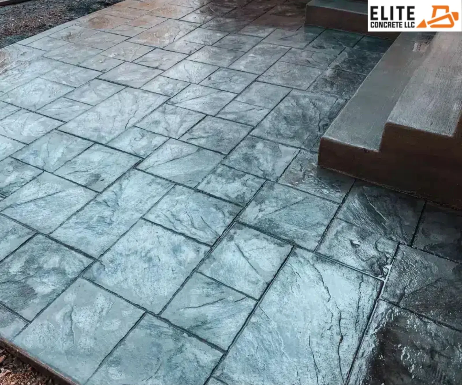 Newly finished slate-grey stamped concrete patio with stone tile patterns next to outdoor stairs.