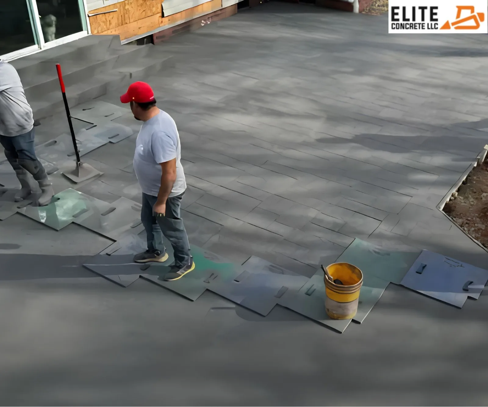 Workers placing texturing mats onto freshly poured concrete for a stamped patio installation.