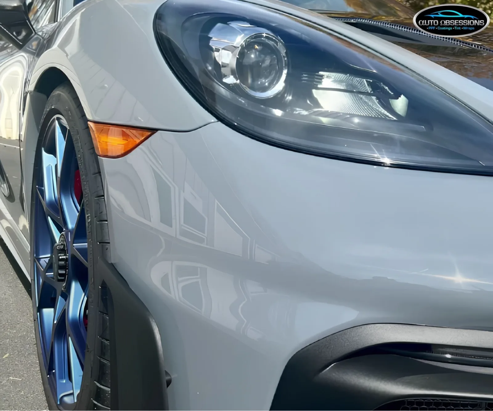 Front fender and headlight close-up of a grey Porsche with glossy paint protection film.