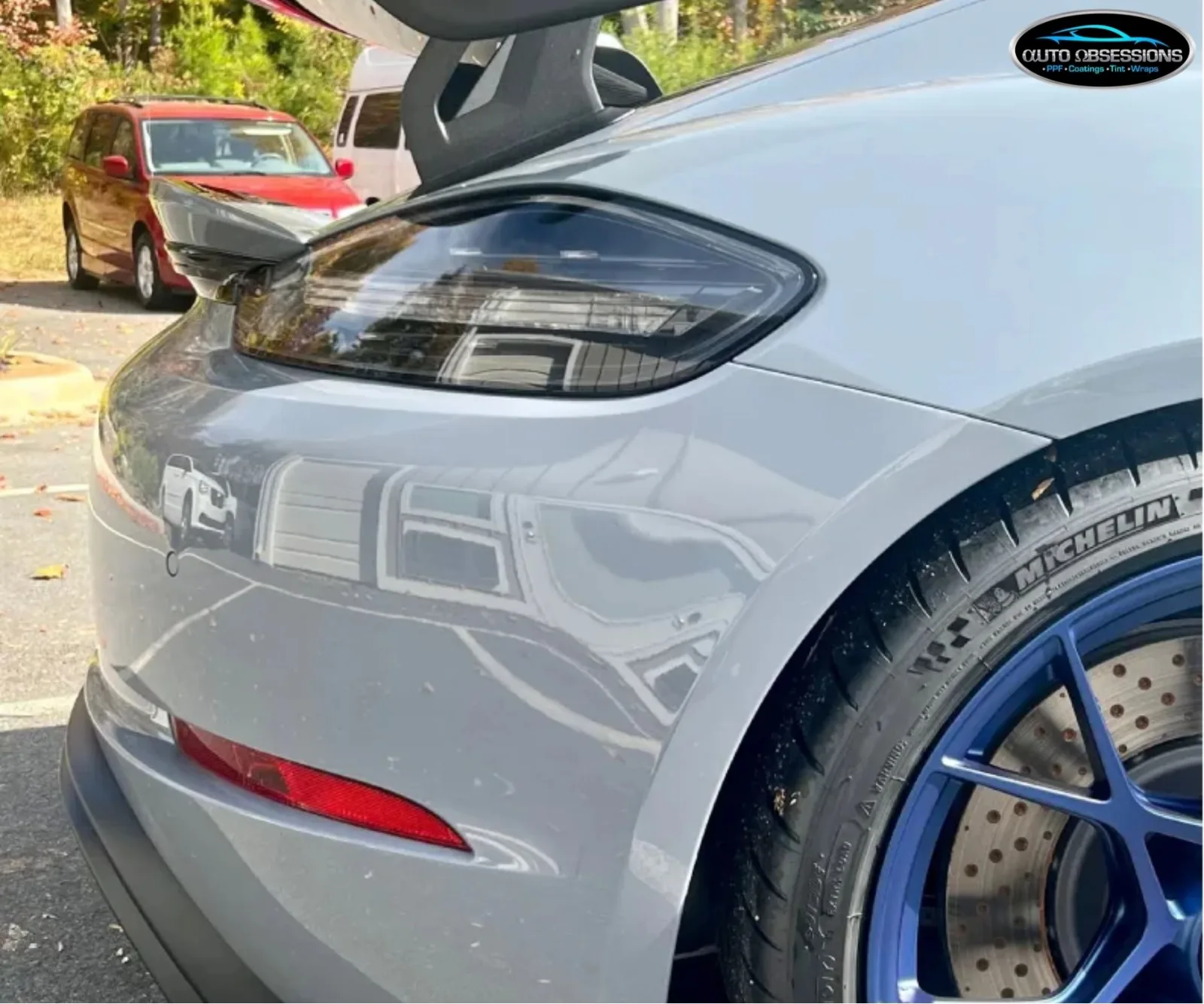 Rear quarter panel and tinted taillight of a grey Porsche with blue wheels.